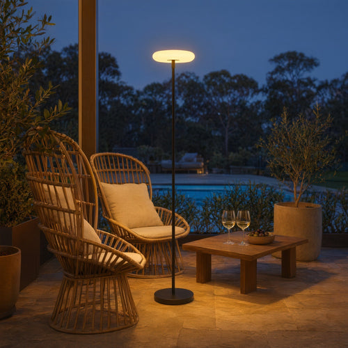 Arco solar cordless floor lamp with a glowing disc on a slim black pole on a terrace at dusk