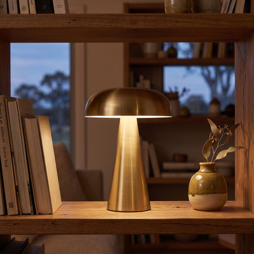 Gold Atlas metal mushroom cordless lamp glowing on a bookshelf in the evening