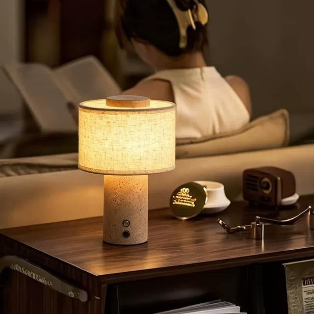 Duna cordless lamp with a travertine base on a bedside table