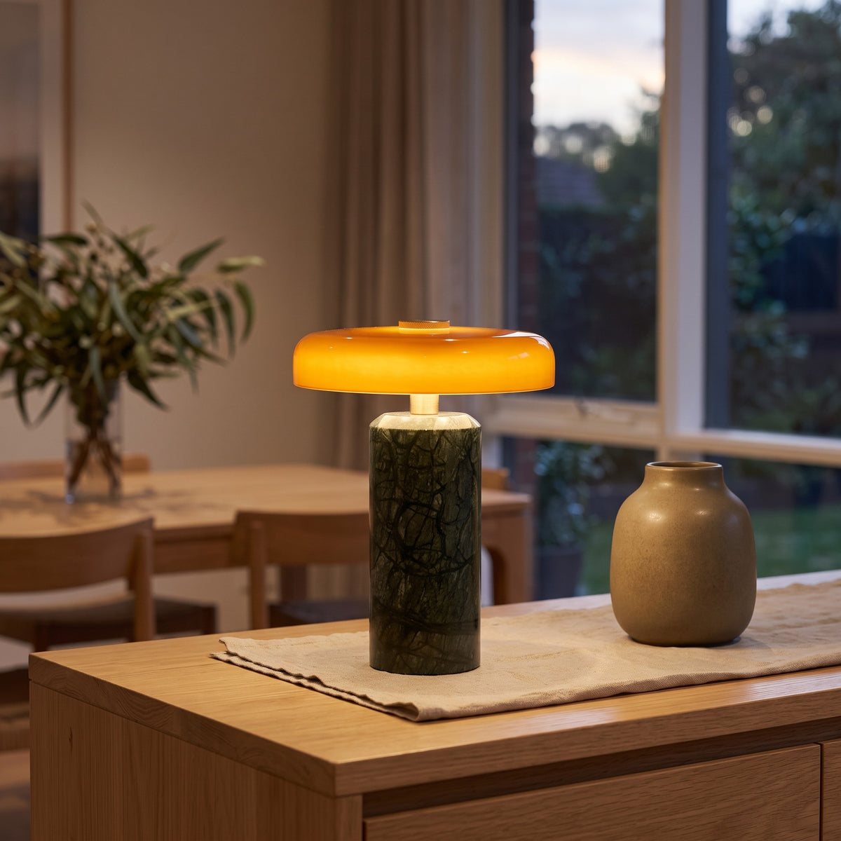 Malaquita cordless lamp with a green marble column and amber glass mushroom shade glowing on a timber sideboard
